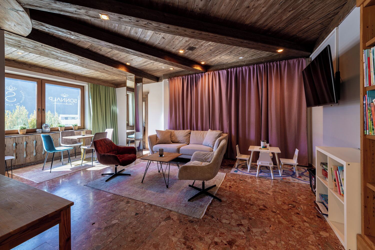 A cozy living area with a wooden ceiling, a sofa, a red chair, a coffee table, and a bookshelf.