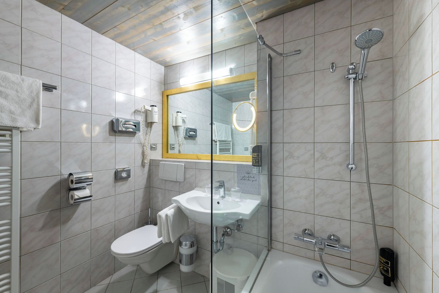 Une salle de bain équipée de toilettes, d’un lavabo, d’une douche et d’un miroir avec un cadre doré.