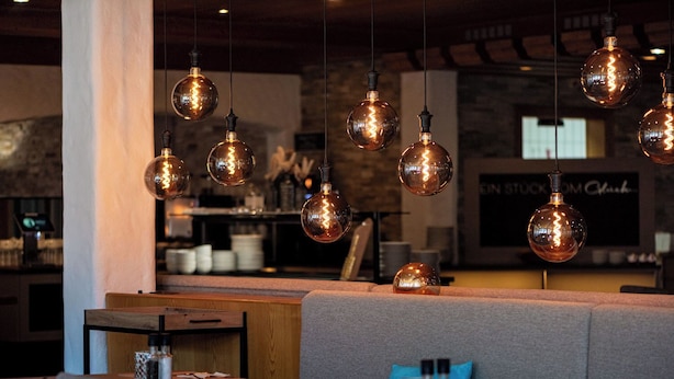 Interior de restaurante con lámparas esféricas colgantes, asientos acolchados y una barra de fondo.