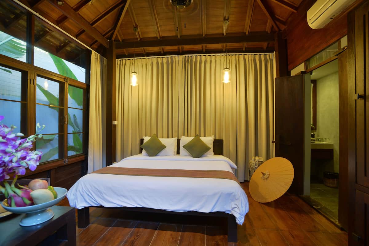 Habitación de hotel con una cama grande, suelo de madera, un frutero y un abanico tradicional.