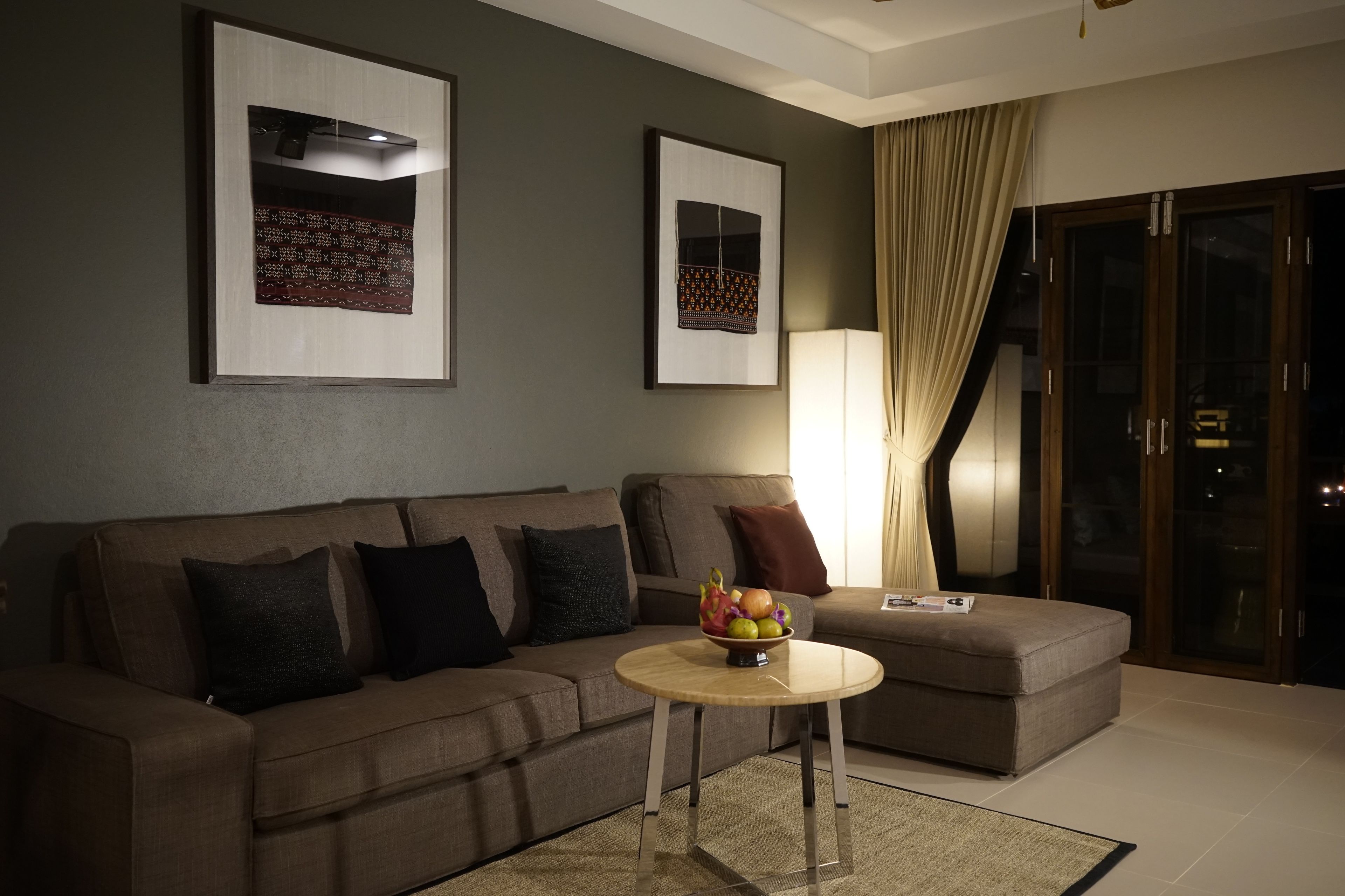 A modern living room with a sofa, a round coffee table with a fruit bowl, and two framed artworks on the wall.