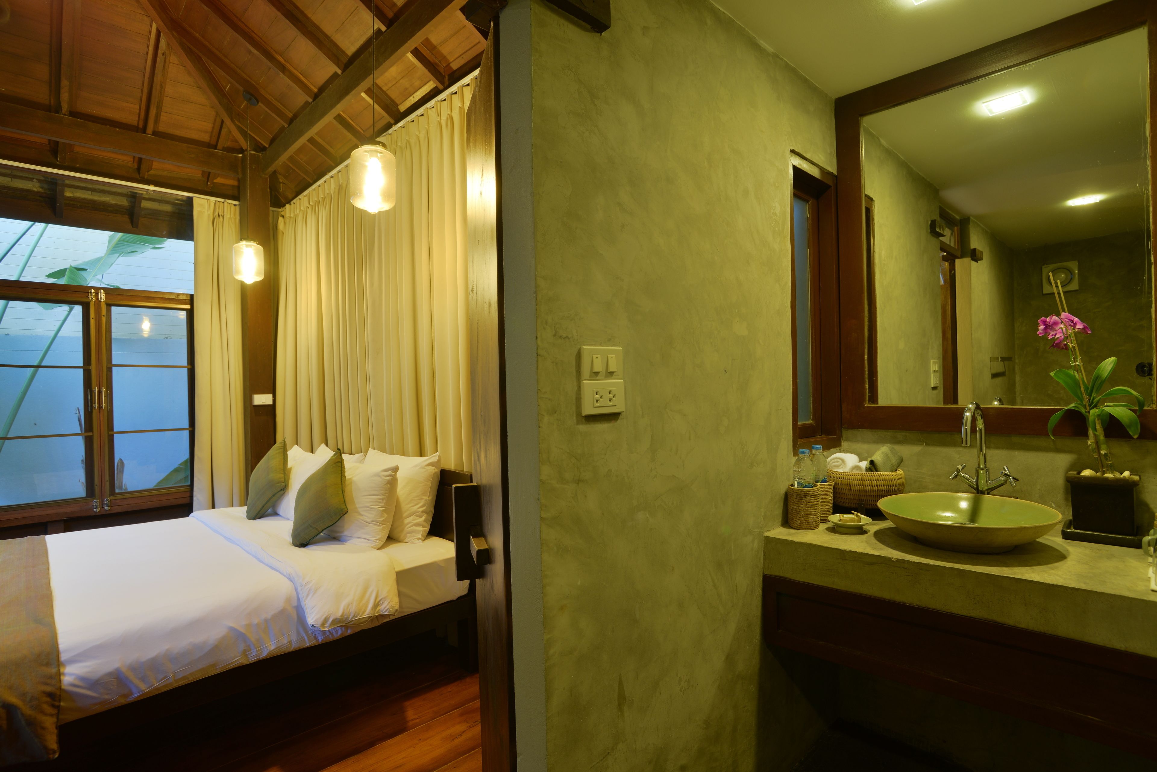 A hotel room with a bed, a bathroom with a sink, and a large window with curtains.