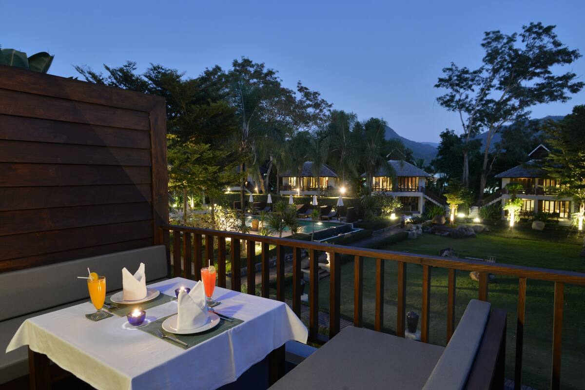 Comedor con una mesa dispuesta para dos, con vistas a una piscina y edificios del complejo.
