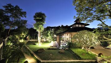 A well-lit garden with a gazebo, pathways, and various plants.