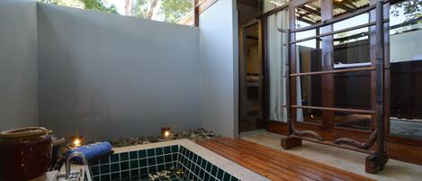 A spa area with a tiled hot tub, wooden deck, and a large window with curtains.