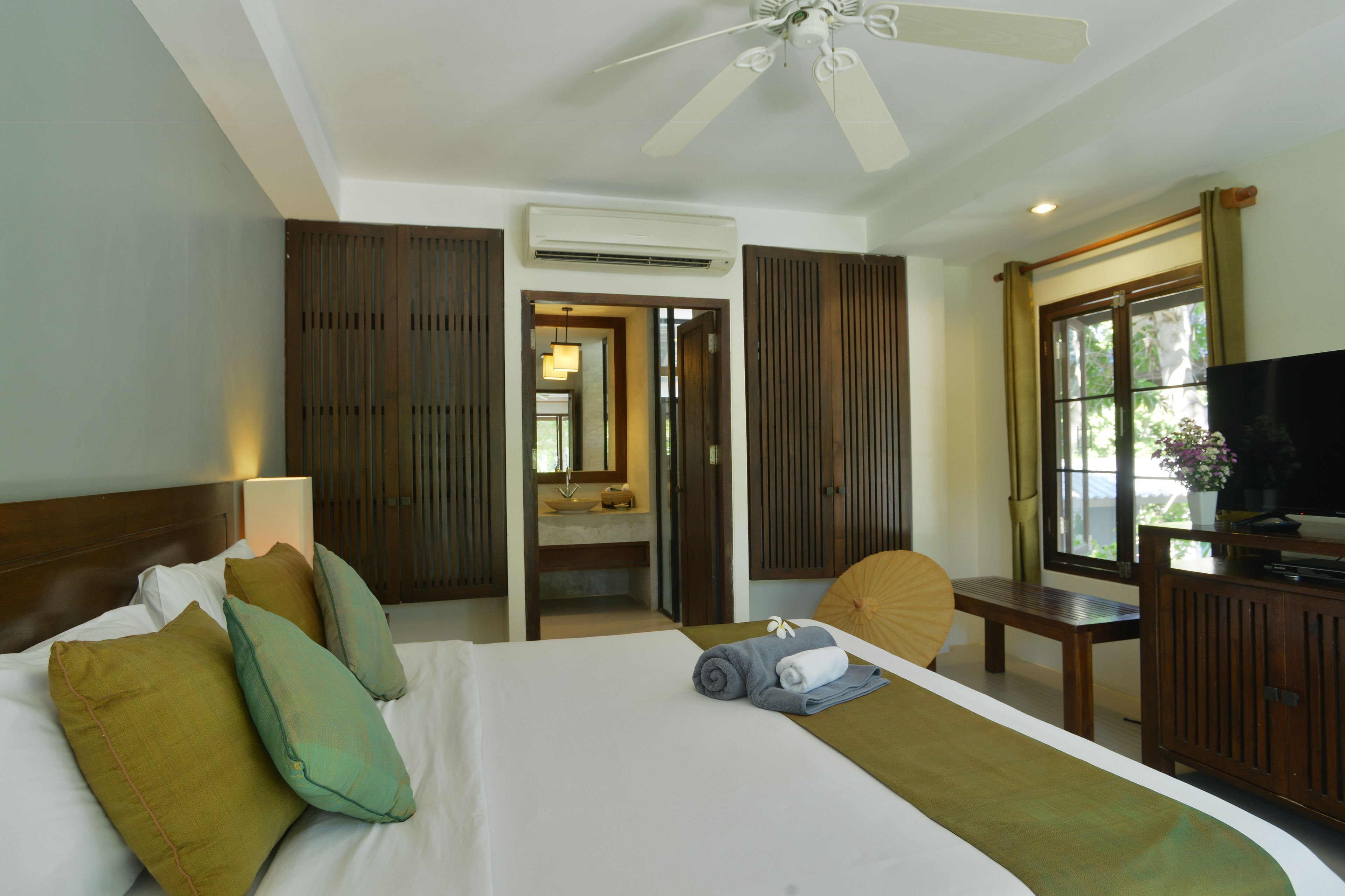 A hotel room with a bed, a desk, a television, and a window with a view of greenery.