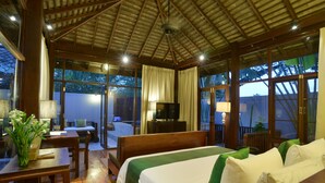 Quarto de hotel com cama, escrivaninha, cadeira, televisão e grandes janelas.