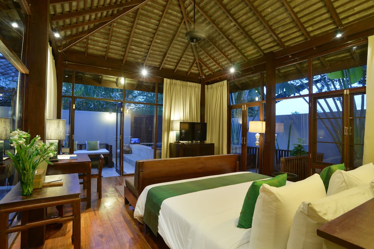 Una habitación de hotel con cama, escritorio, silla, televisión y ventanas amplias.
