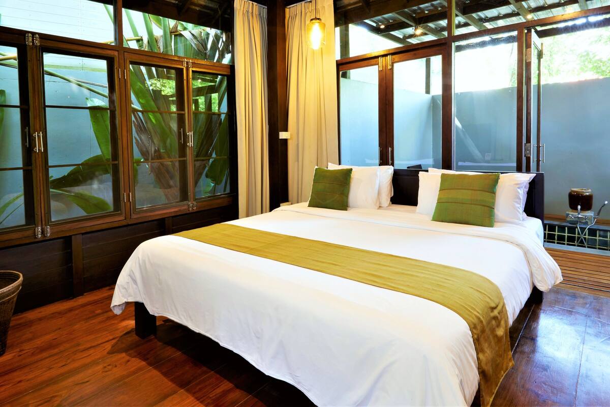 Habitación de hotel con una cama grande, suelo de madera y ventanas amplias con cortinas.