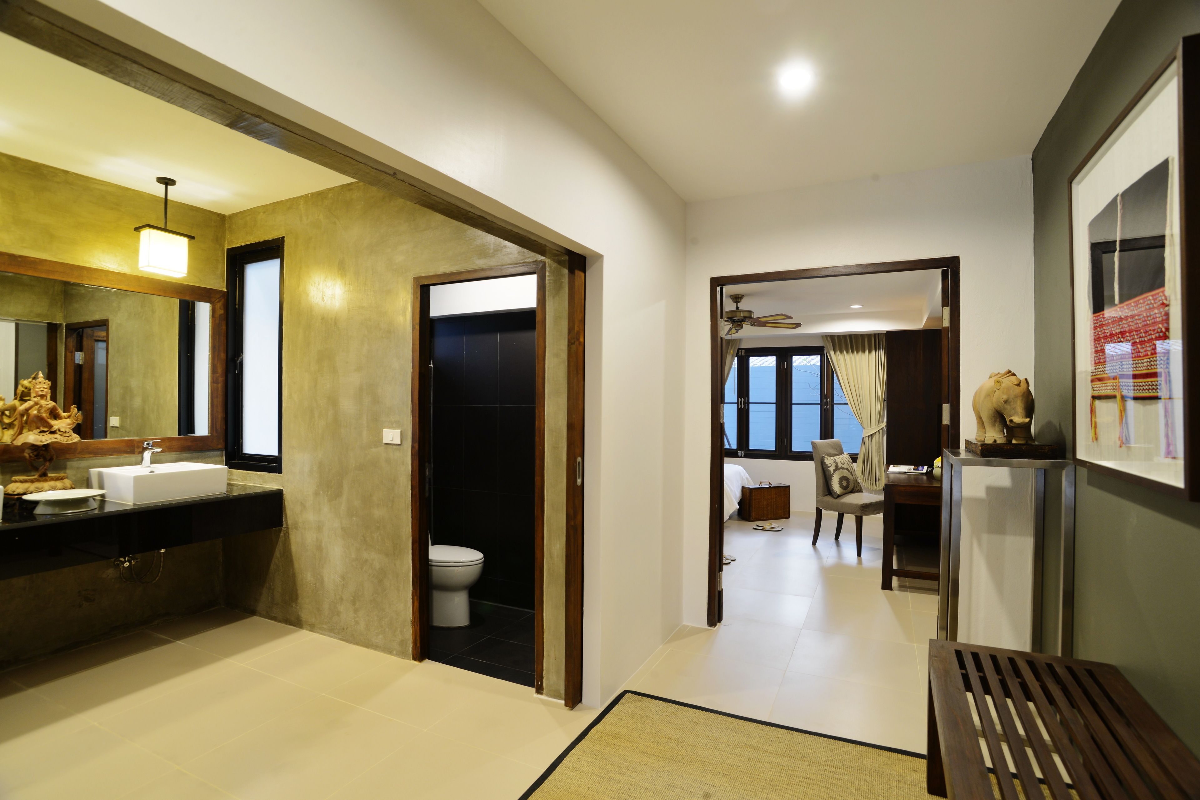 A modern bathroom with a sink, toilet, and shower. There is a wooden bench and a chair in the room.