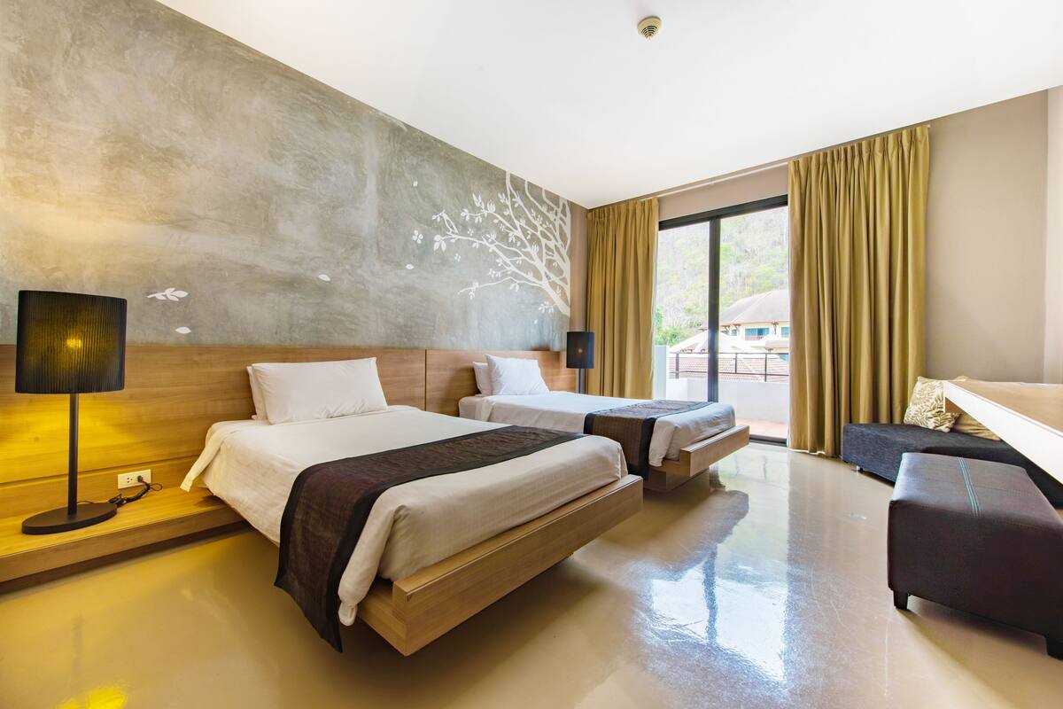 A hotel room with two beds, a sofa, a lamp, and a large window with curtains.