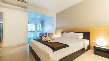 A modern hotel room with a large bed, a bedside table with a lamp, and a view of the outside through a window.