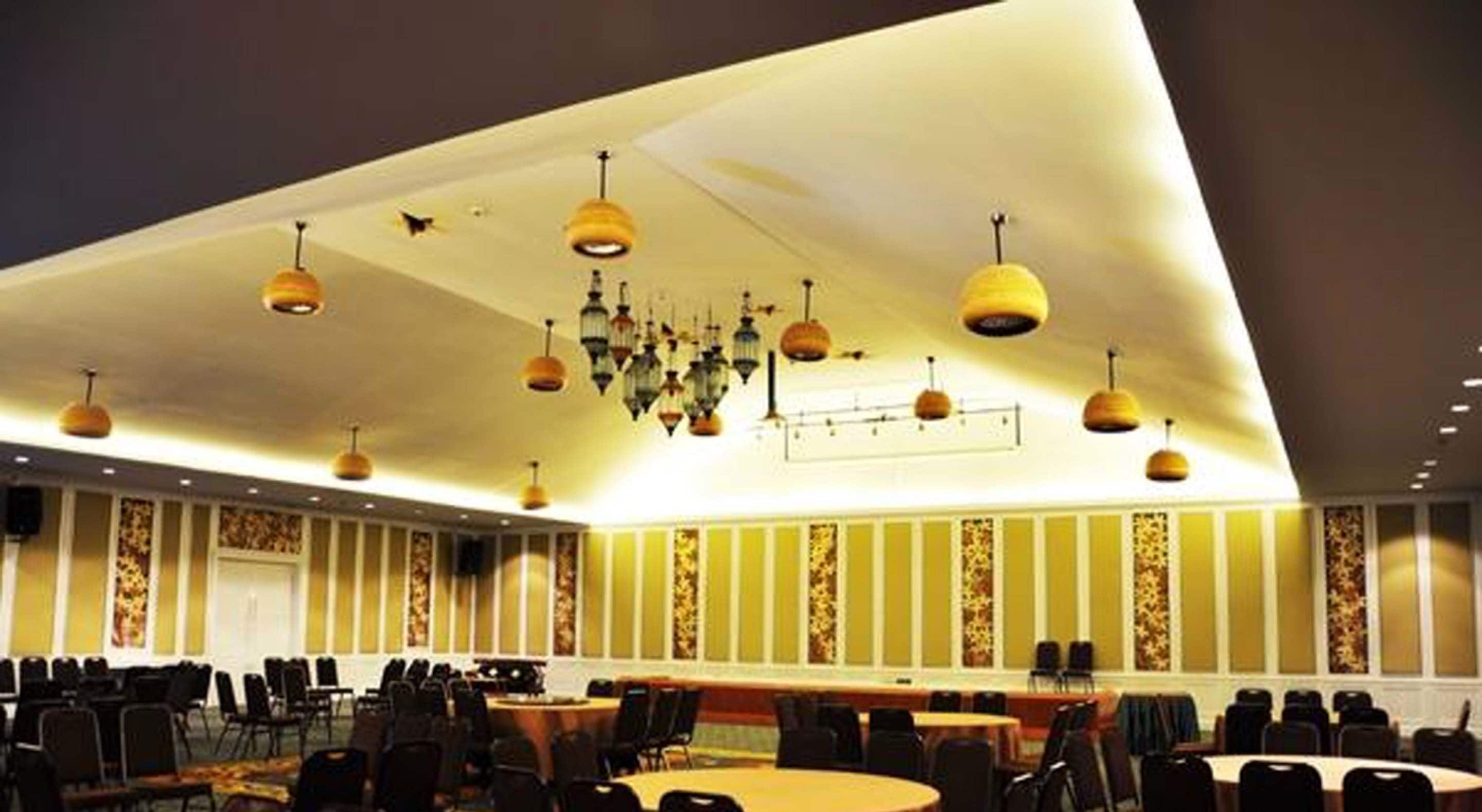 Un salón de conferencias con varias mesas y sillas, luminarias decorativas en el techo y paneles de pared con diseños.