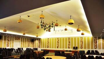 Un salón de conferencias con varias mesas y sillas, luminarias decorativas en el techo y paneles de pared con diseños.