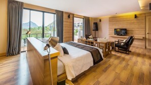 A hotel room with a large bed, a desk with a lamp, a TV, and a view of mountains. - The Greenery Resort Khao Yai (Pak Chong)