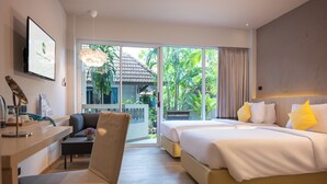 Une chambre d’hôtel avec un lit, un bureau et une chaise. Une grande fenêtre offre une vue sur la verdure environnante.