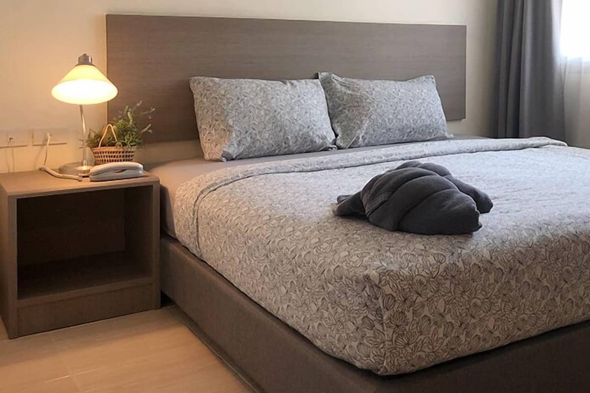 Una cama bien hecha con una colcha de estampado floral, una lámpara de noche y una mesita de noche con una planta.