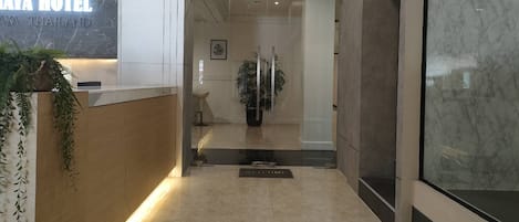 Zona de recepción de un hotel con un mostrador de mármol, puerta de entrada de vidrio y una planta en maceta.