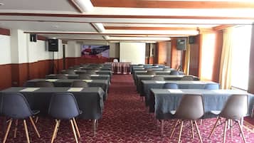 A conference room with rows of tables and chairs, a red carpet, and a banner on the wall.
