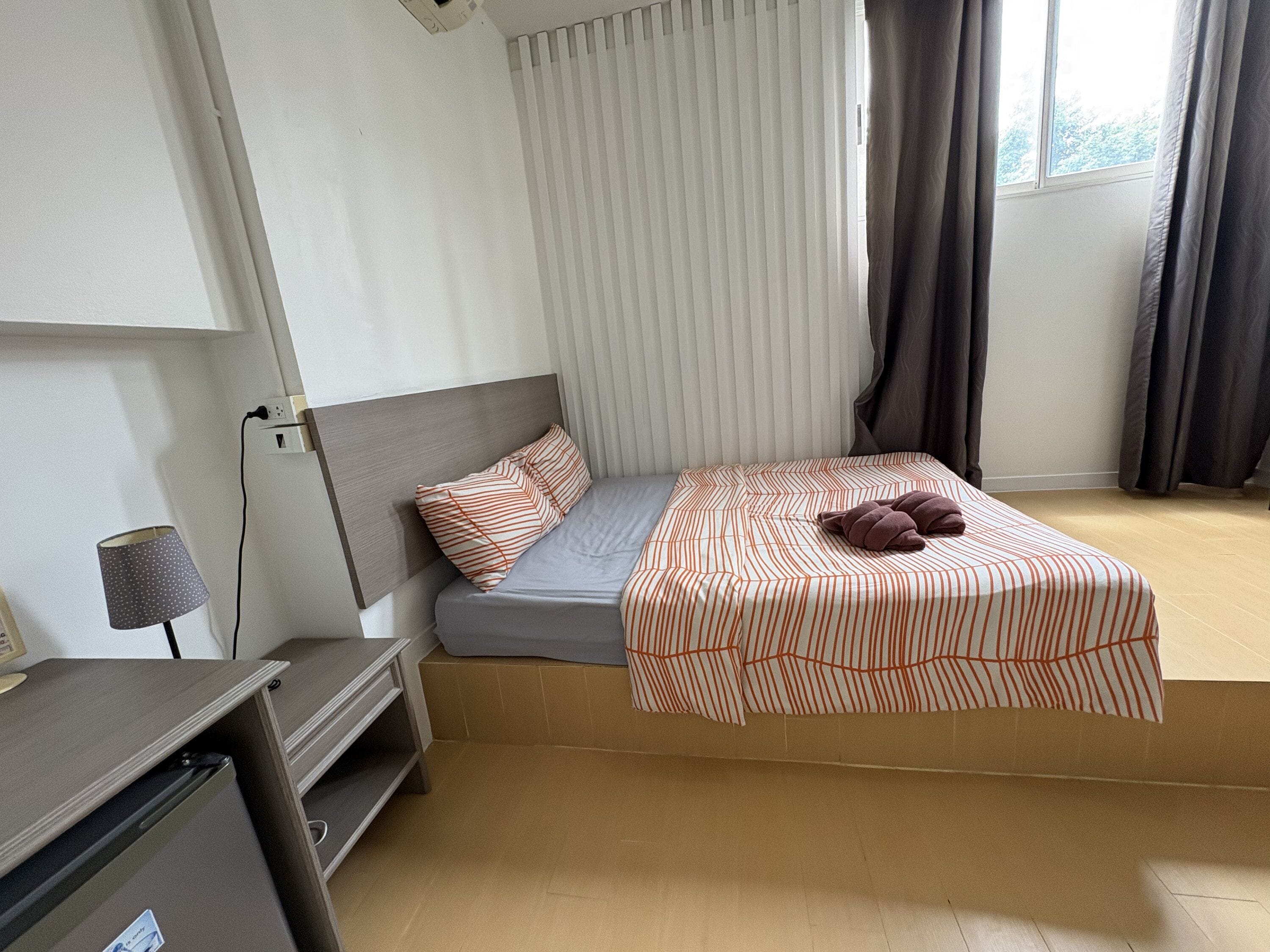 Un dormitorio con cama, escritorio, lámpara y ventana con cortinas.
