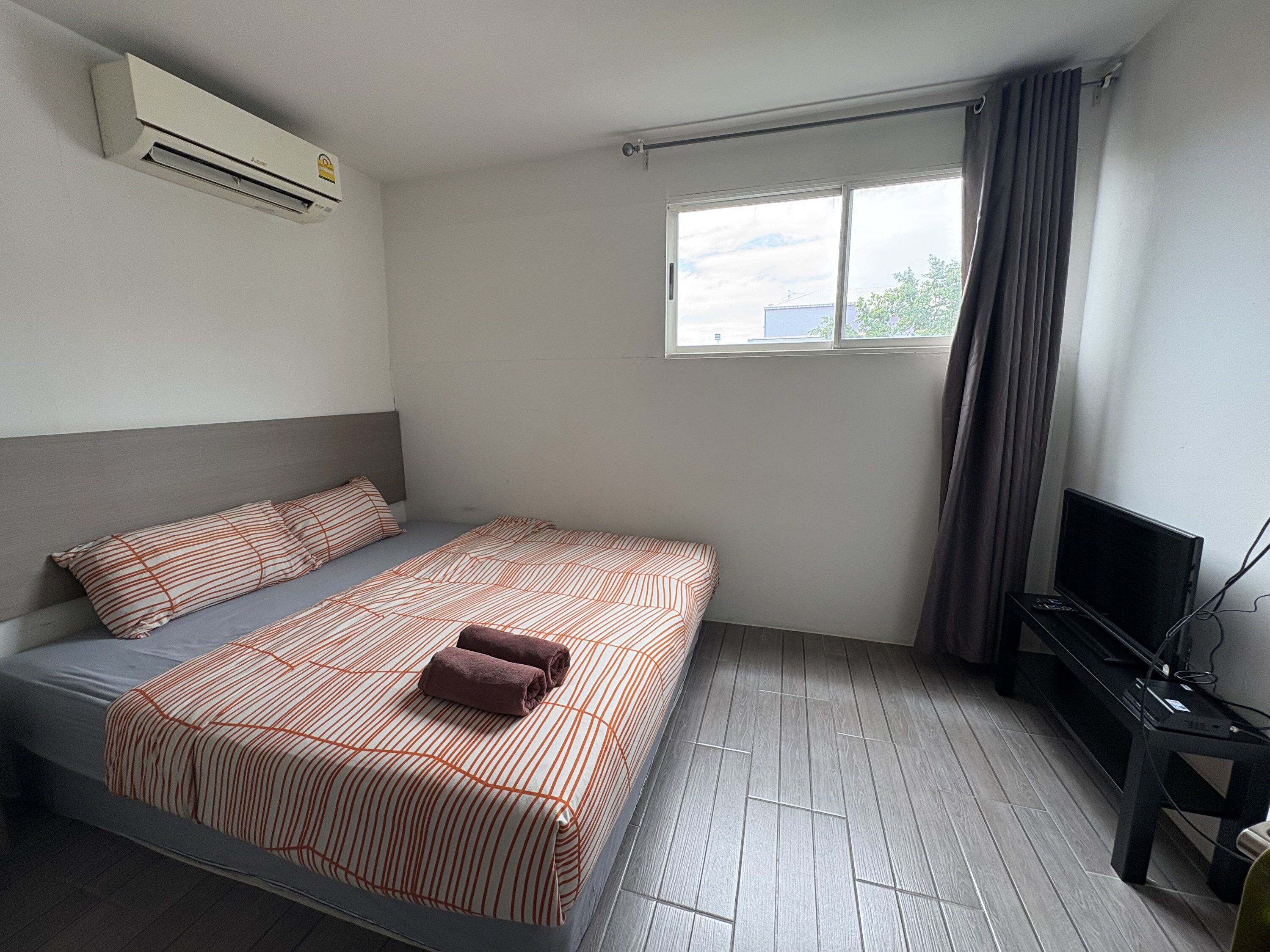 Une chambre d’hôtel équipée d’un lit, d’une télévision, d’une fenêtre avec des rideaux et d’un appareil de climatisation.