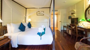 A four-poster bed with white linens and blue pillows, a wooden desk with a chair, and a television in a hotel room. - Buddy Lodge (Bangkok)