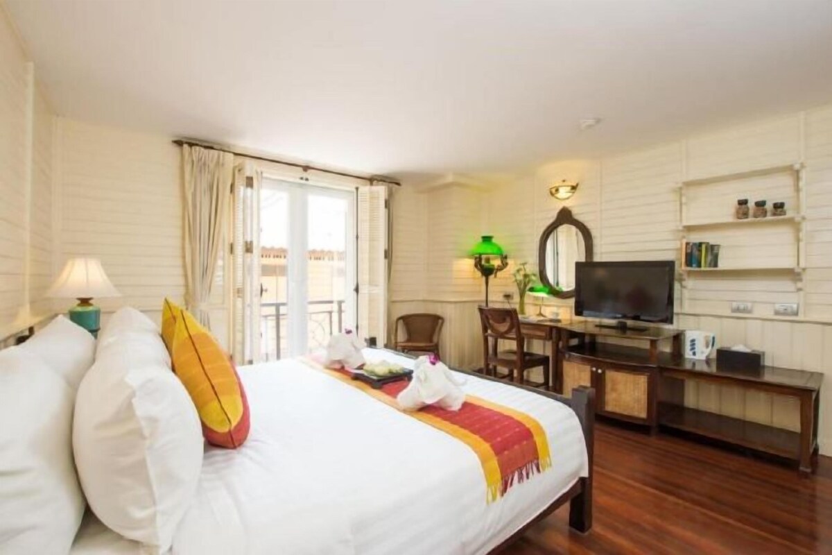 A hotel room with a bed, a desk with a television, a chair, and a bookshelf.