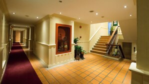 A hotel hallway with a red carpet, tiled floor, a staircase with a railing, and a door with a window. - Buddy Lodge (Bangkok)