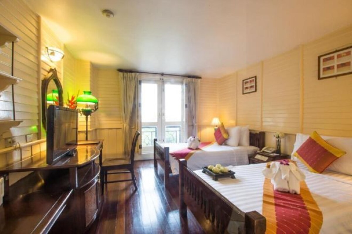 Een hotelkamer met een houten bureau, twee bedden, een raam met gordijnen en uitzicht op de omgeving.