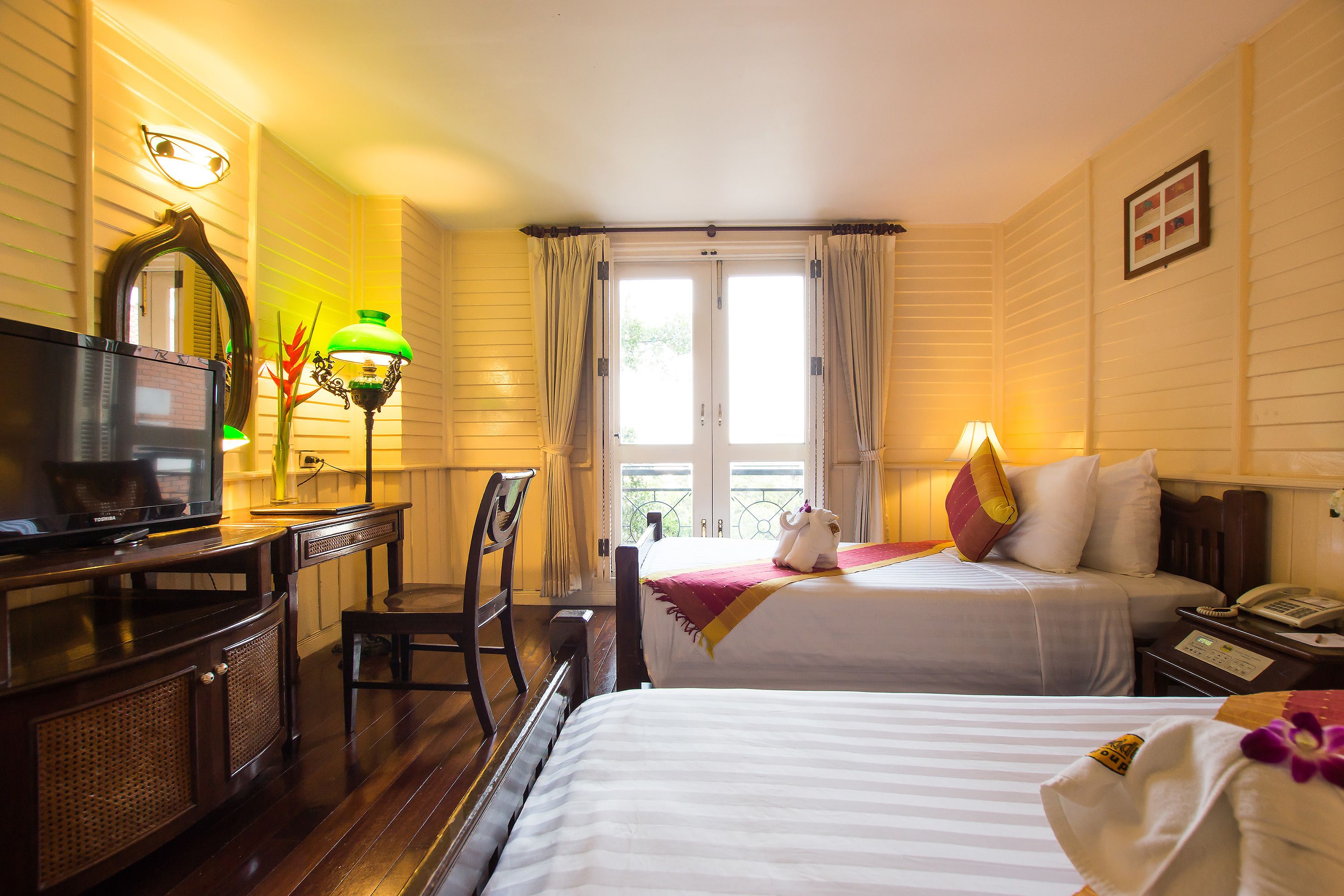 A hotel room with two beds, a desk with a television, a chair, and a window with curtains.