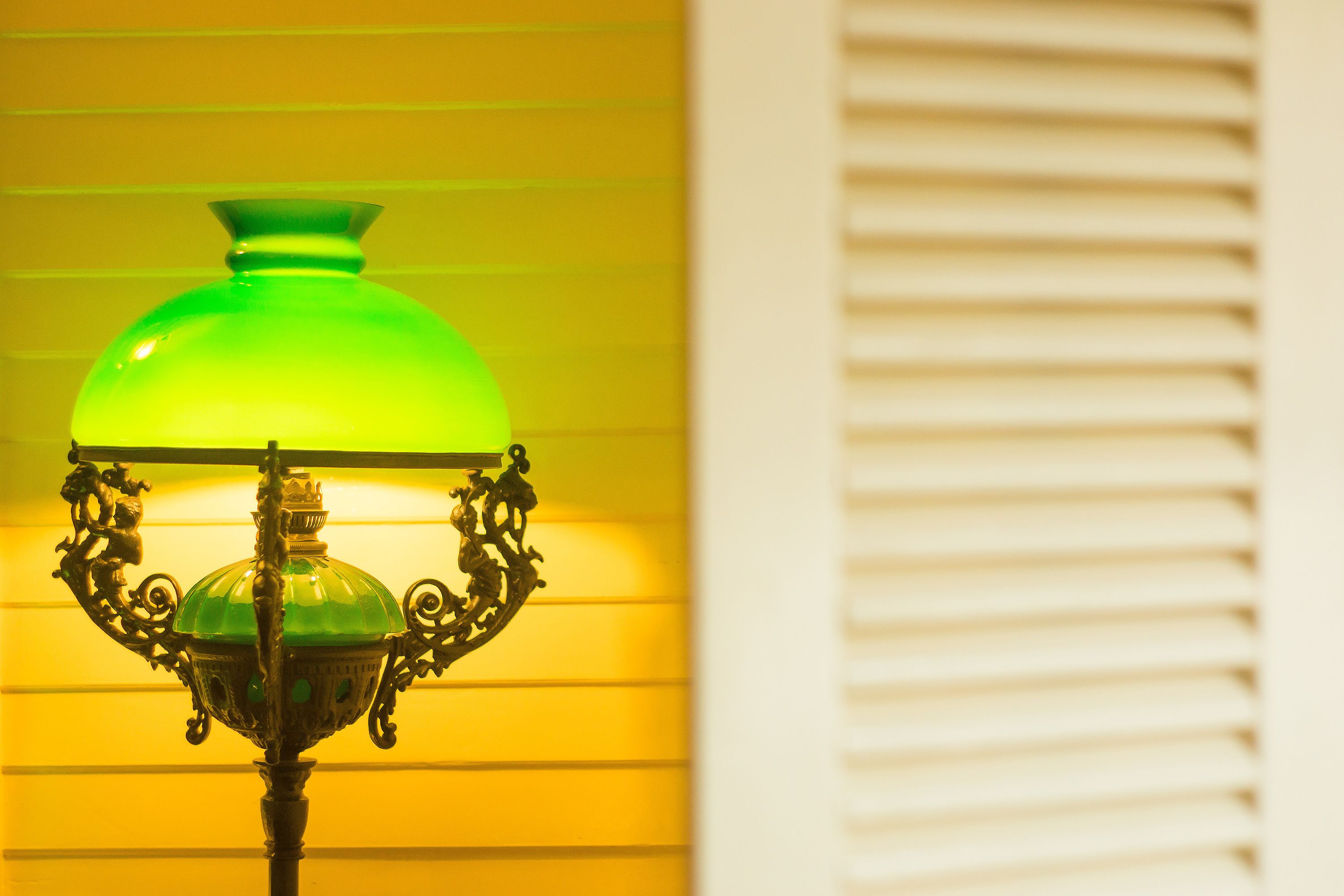 A green glass lamp with ornate metalwork against a yellow background.