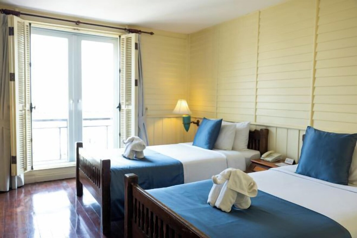 Ein Hotelzimmer mit zwei Betten, einer Lampe, einem Telefon und Blick durch ein Fenster mit Rollläden.