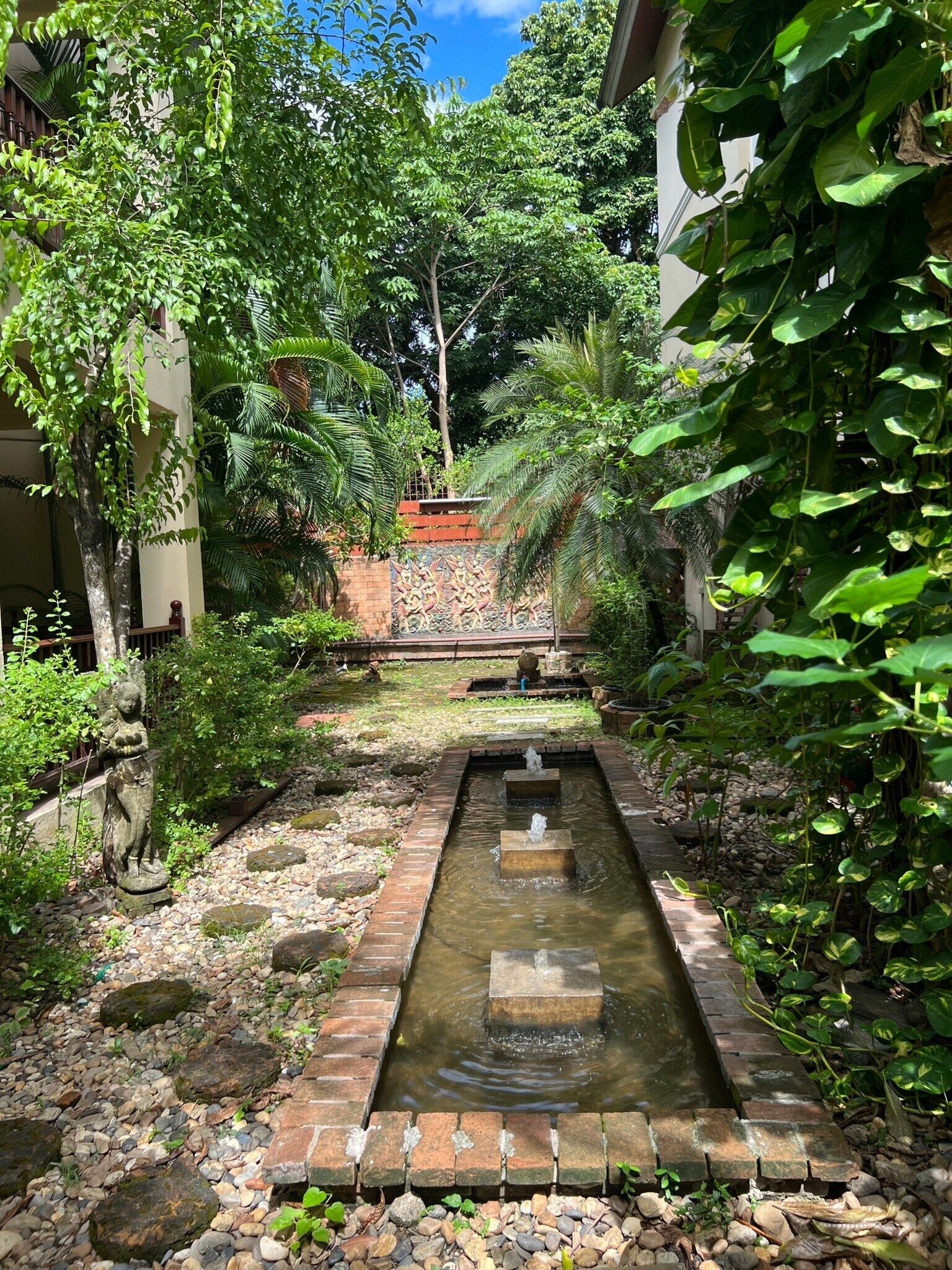 A serene garden with a rectangular water feature, surrounded by lush greenery and a decorative wall.