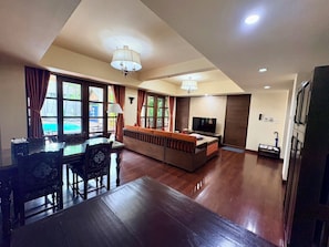 A spacious living area with a dining table, sofa, TV, and large windows. - Shewe Wana Suite Resort (Chiang Mai)
