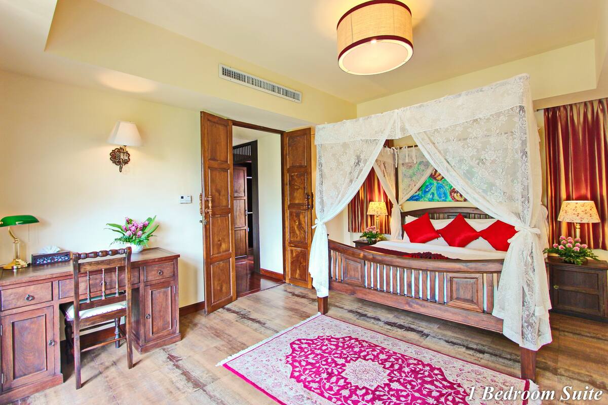 A bedroom with a four-poster bed, wooden furniture, and a decorative rug.