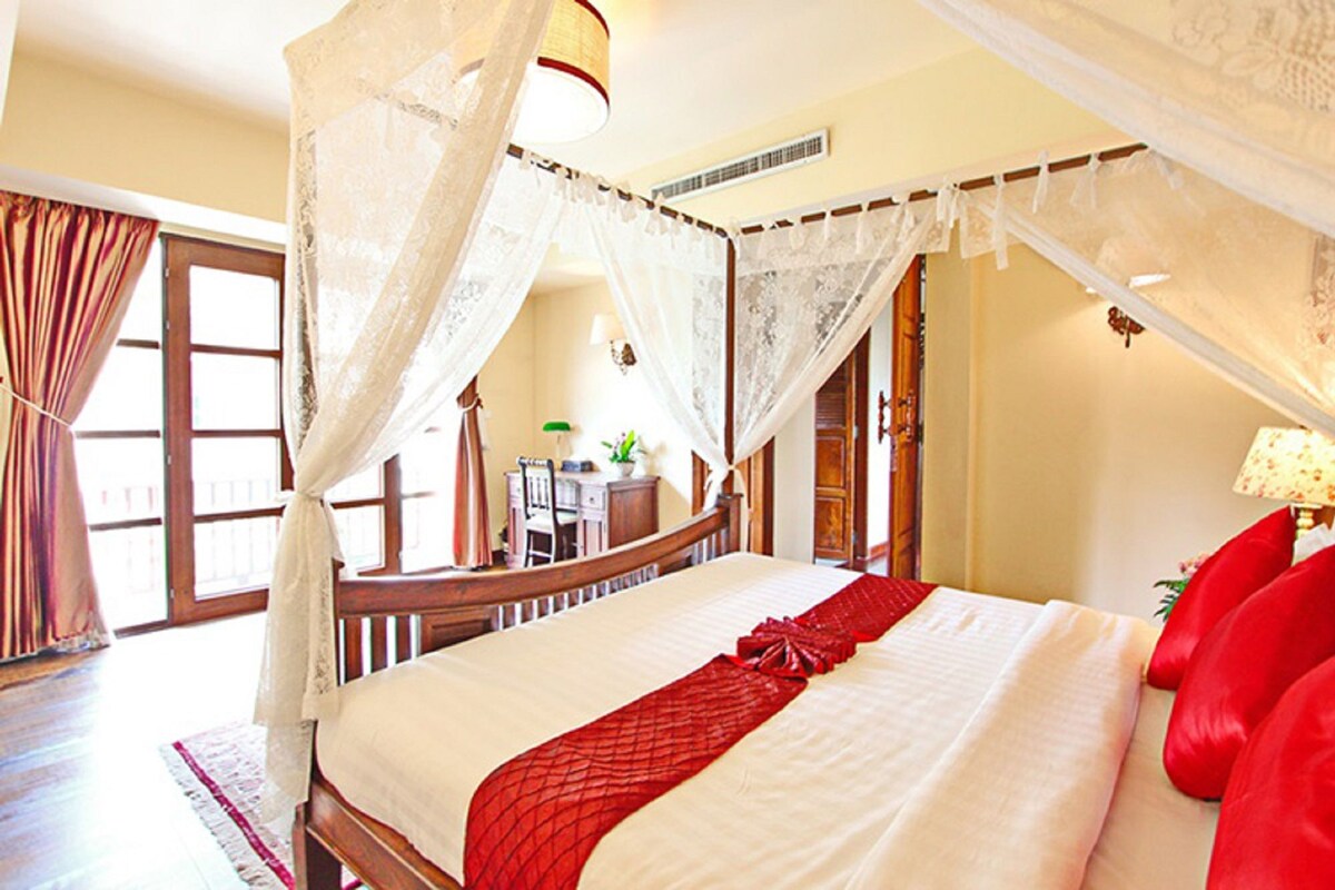 A bedroom with a four-poster bed, a red bedspread, and a canopy.