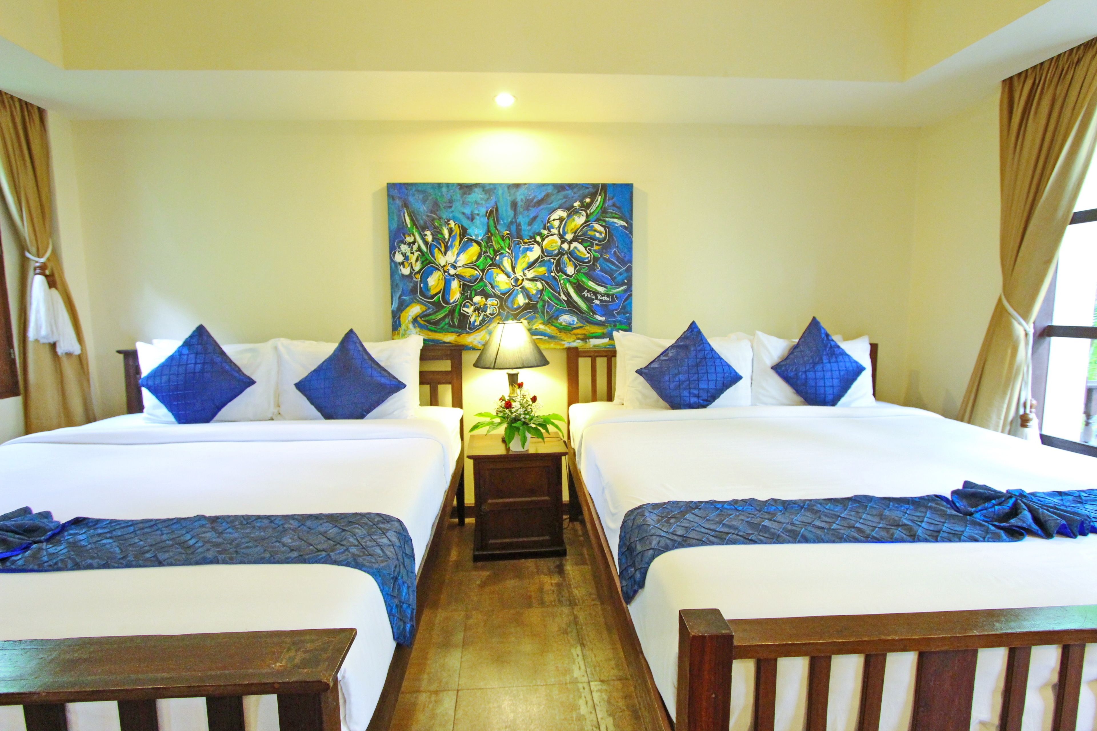 A hotel room with two beds, a painting on the wall, a nightstand with a lamp, and a window with curtains.