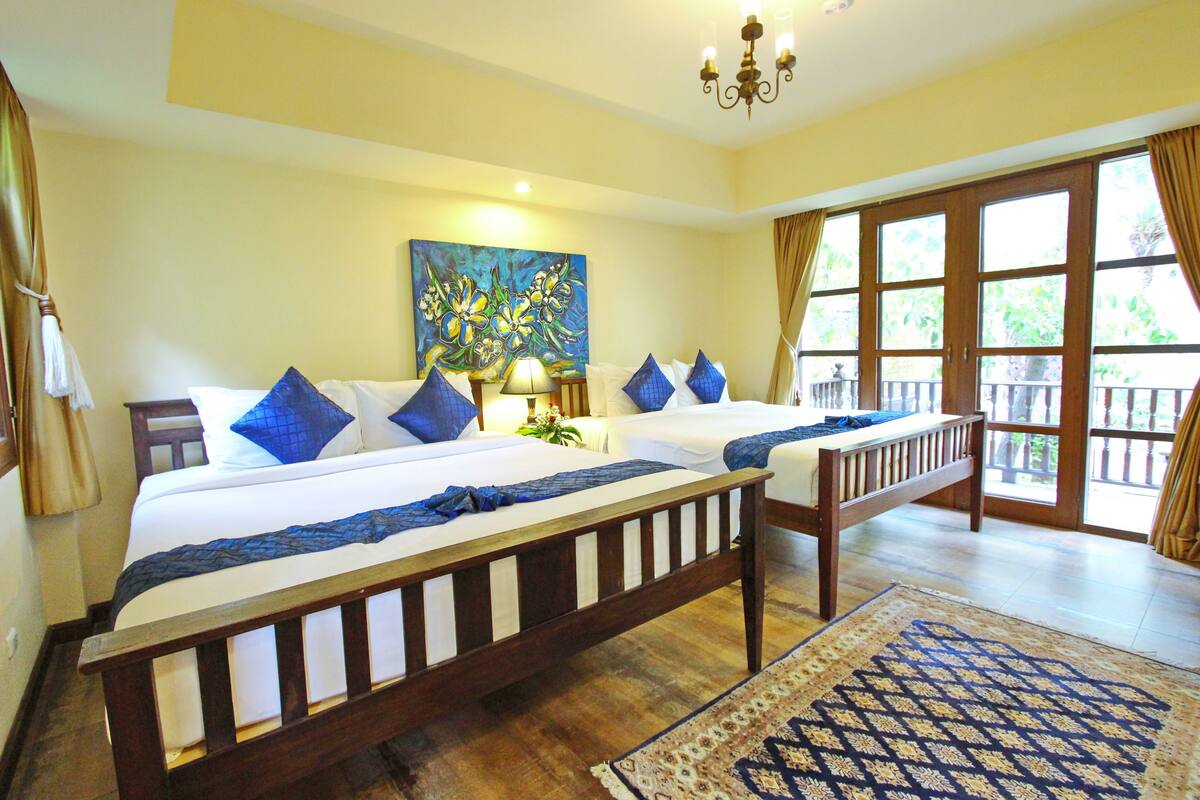 A hotel room with two beds, a large window, a chandelier, and a painting on the wall.