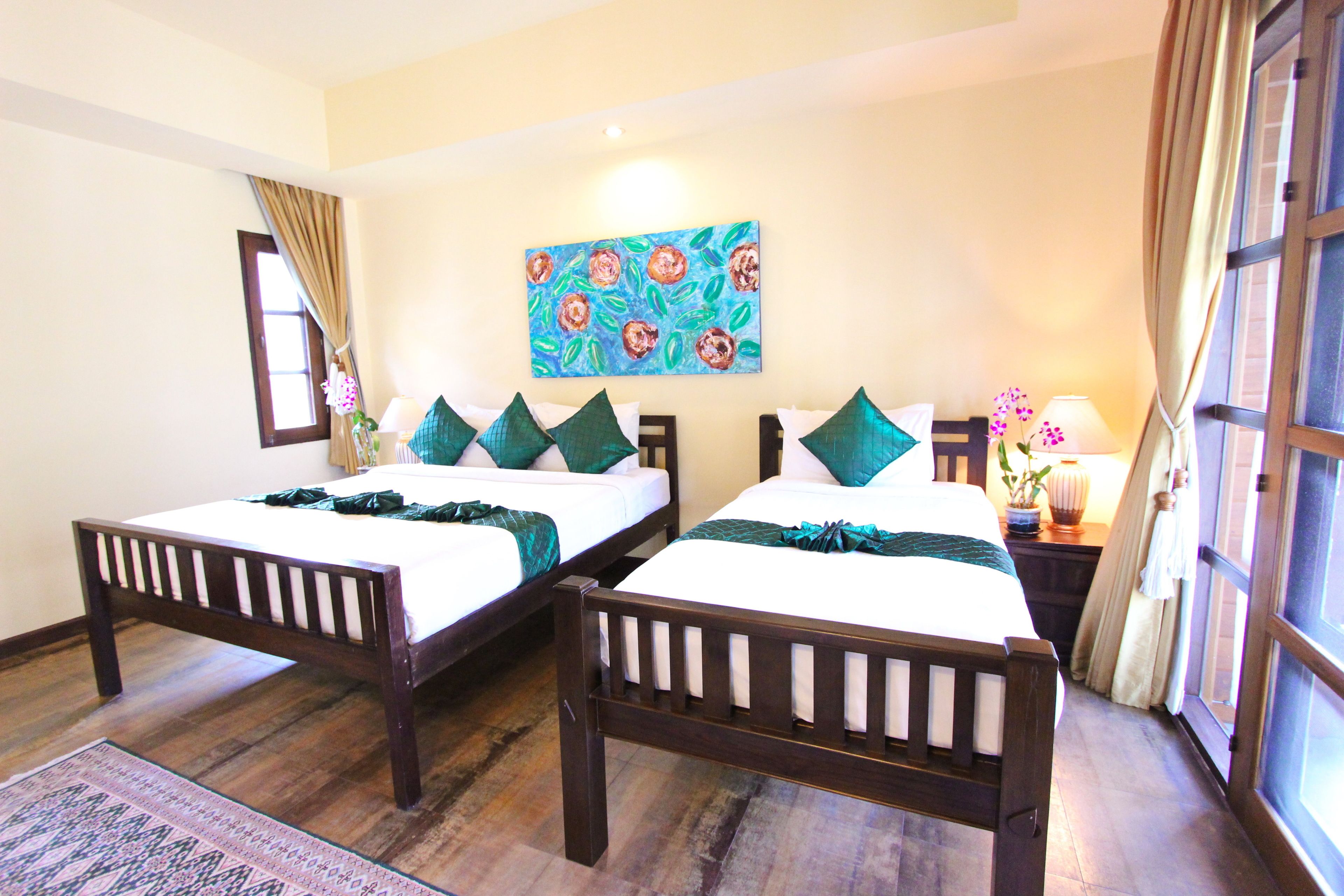 A hotel room with two wooden beds, a painting on the wall, and a window with curtains.