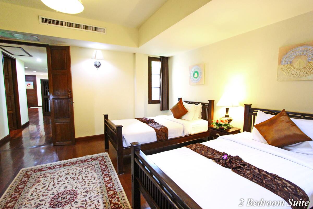 A 2-bedroom suite with two beds, a wooden floor, a patterned rug, and a wall clock.
