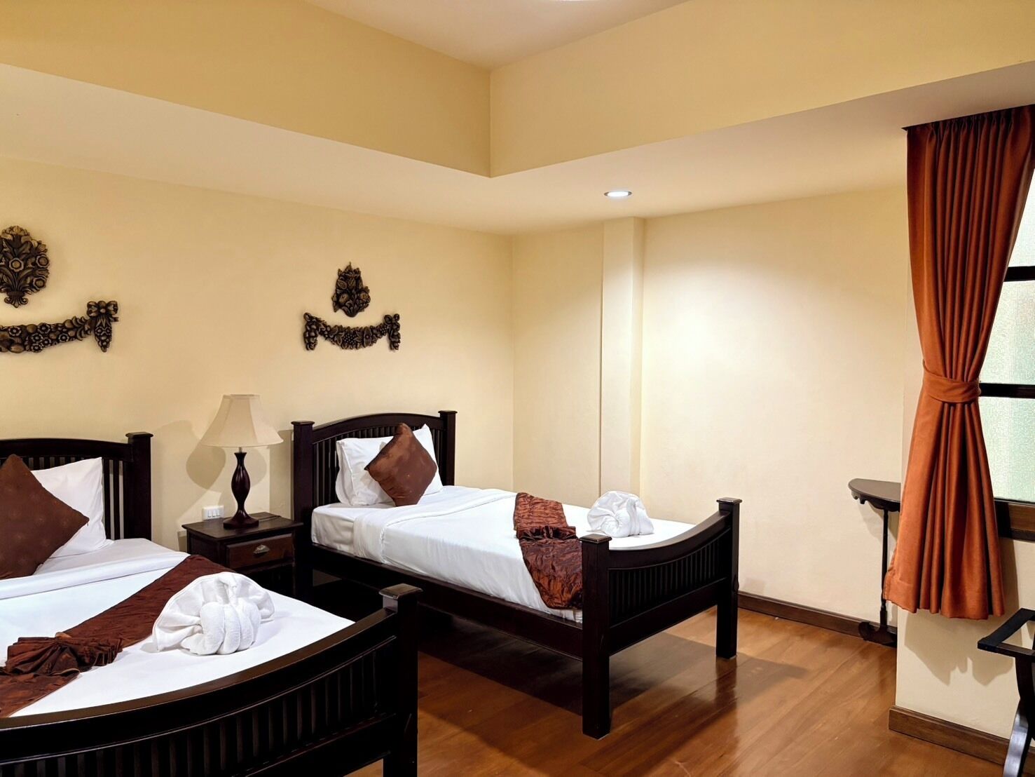 A hotel room with two beds, a nightstand, a lamp, and a window with curtains.
