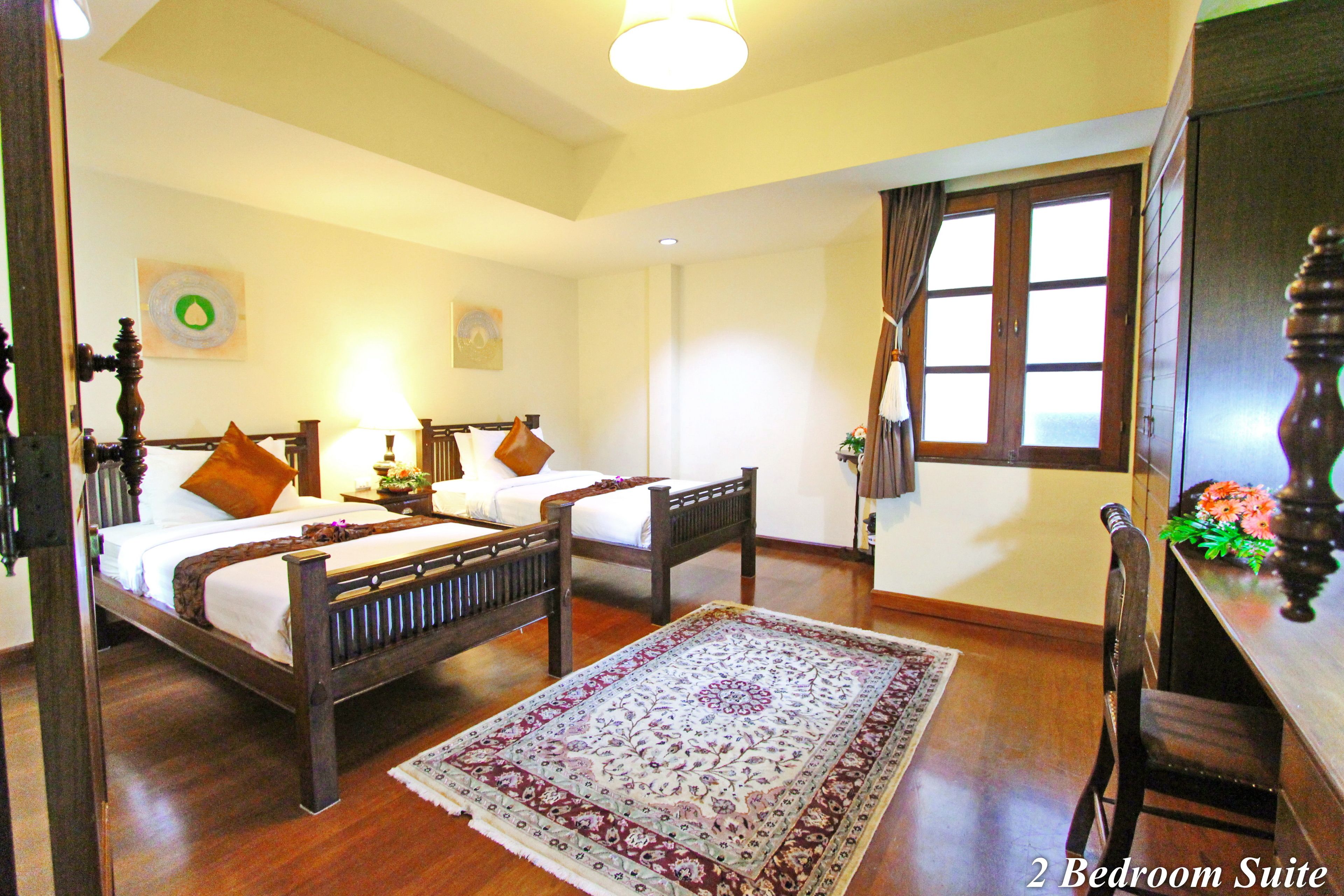 A 2-bedroom suite with two wooden beds, a large decorative rug, and a wooden desk with a chair.