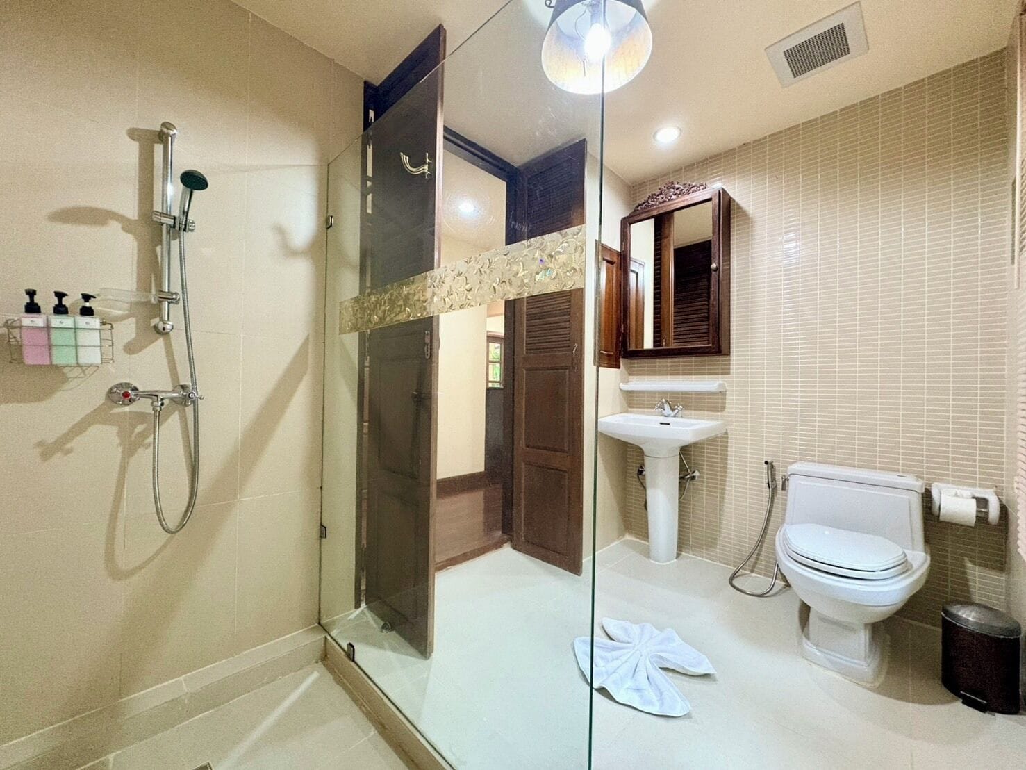 Un baño con cabina de ducha de vidrio, un lavamanos blanco, un inodoro y un espejo sobre el lavamanos.