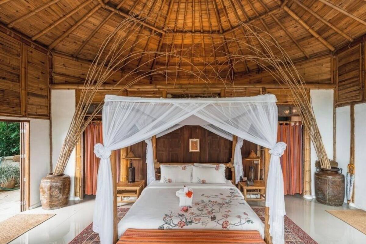 A room with a bed under a canopy, wooden walls, and a thatched roof.