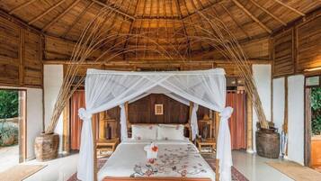 A room with a bed under a canopy, wooden walls, and a thatched roof.