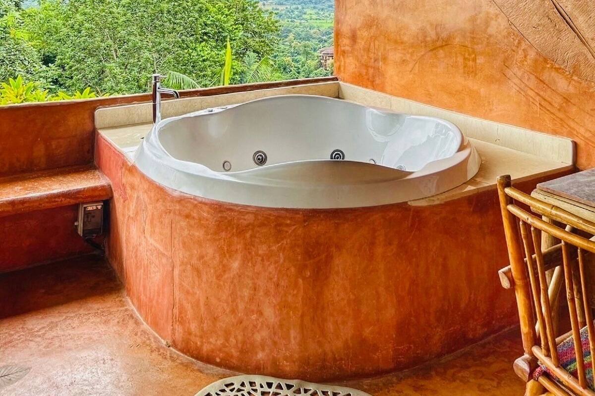 A hot tub in a room with a view of lush greenery and mountains.
