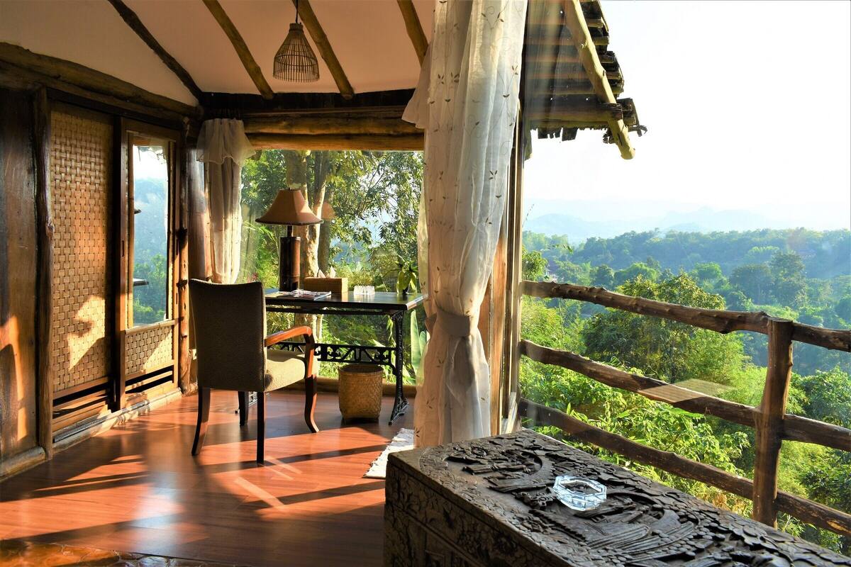 A wooden deck with a table and chairs, a decorative table centerpiece, and a view of lush greenery.
