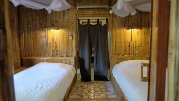 A room with two beds, a bamboo wall, a stone-patterned floor, and a canopy over the beds.
