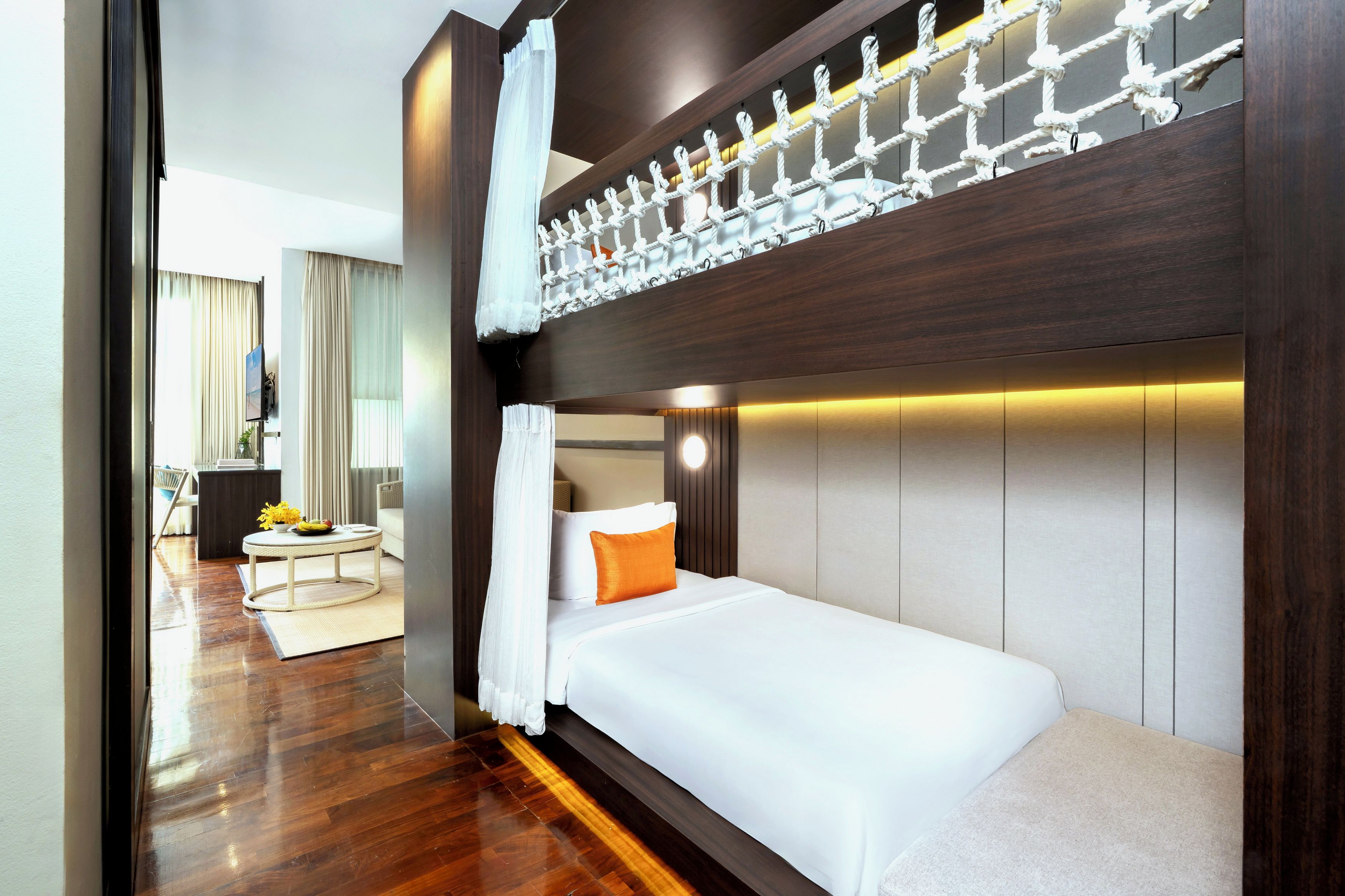 A hotel room with a bunk bed, a bedside table, a chair, and a view of the hallway.