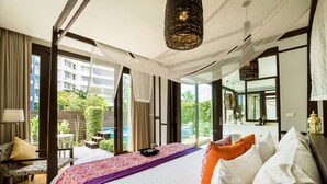 A hotel room with a large bed, a sitting area with a chair and a small table, a balcony with a pool, and a view of greenery and buildings. - The Rock Hua Hin Beachfront Spa Resort (Hua Hin)